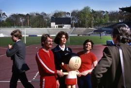 Iona Campagnolo with two unknown people holding a mascot on a running track in Germany