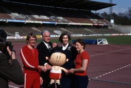 Iona Campagnolo with three unknown people holding a mascot on a running track in Germany