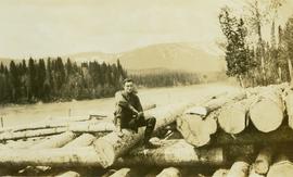 Man sitting on top of a large log pile