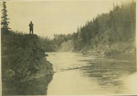 Unidentified man standing on a rocky cliff above a river