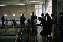 Iona Campagnolo laughing while interacting with a young female swimmer at an aquatic centre in East Germany