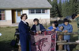 Iona Campagnolo standing with children by a blanket depicting First Nations whale art