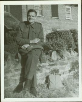 James Joseph Claxton in uniform seated on a garden wall