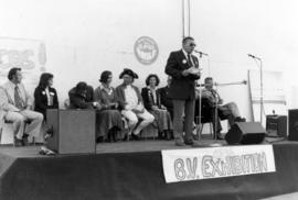 Man at microphone with Iona Campagnolo, Deputy Premier Grace McCarthy, and others in background at the 48th Bulkley Valley Exhibition in Smithers