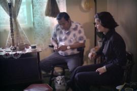 Iona Campagnolo and First Nations man sitting in living room with small dog
