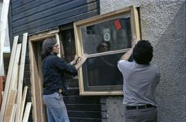 Assistant to Iona Campagnolo and man install a window in a house under construction