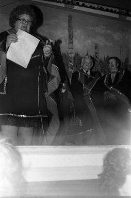 Men on stage with a woman, possibly Ada Yovanovich or Blanche MacDonald, wearing button blankets in Skidegate