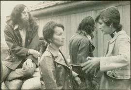Unidentified man and woman talking to Iona Campagnolo in front of a Tsimshian longhouse