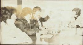 Two unidentified men and Iona Campagnolo sit around a table listening to an unidentified woman