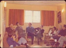 M.P. Iona Campagnolo talking to nine unidentified individuals seated inside a curtained room, ca. 1975