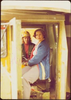 M.P. Iona Campagnolo poses in the cab of mining truck with a female operator wearing a “Naranda” hard hat