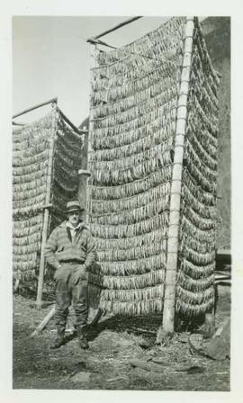 Mr. Huston stands in front of two tall racks of drying eulachon