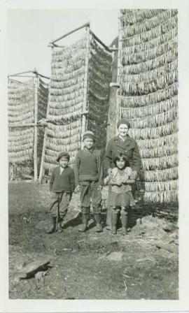 Mrs. Huston stands with three First Nations children in front of three tall racks of drying eulachon