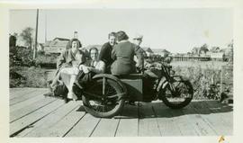 Five people ride a motorcycle and sidecar along the Port Simpson boardwalk