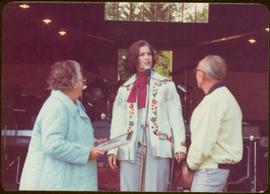 Commonwealth Games, Edmonton 1978 - Iona Campagnolo speaks into microphone beside unidentified man and woman