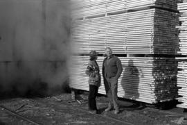 Iona Campagnolo with hard hat speaking with man in front of wood at sawmill owned by Rim Forest Products in Hazelton