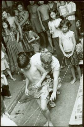 CUSO Mission, North-eastern Thailand - Unidentified boy walks between strings attached to a young girl as crowd looks on