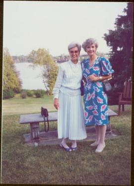 Iona Campagnolo and unidentified woman stand at stone bench overlooking a lake