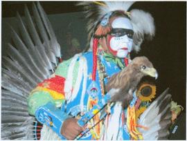 Unidentified man in full regalia adorned with white, black and red face paint, holding a staff displaying an eagle head