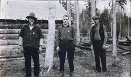 Three men standing in front of a log cabin