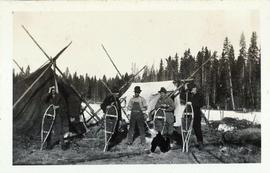 Four men standing with snowshoes in front of tents