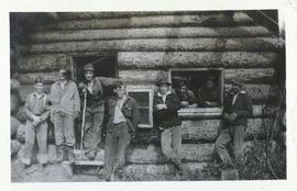 Several men standing around and in a log cabin