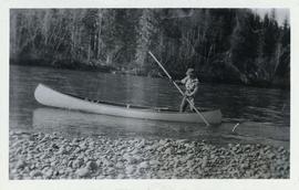 A man using a large pole to steer his canoe up a river
