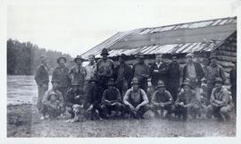 Several men, a boy and a dog in front of a cabin