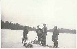Four men standing next to sleds