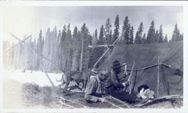 Two men and a dog sitting in front of a tent