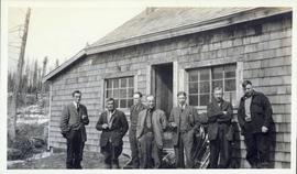 Several men standing in front of a shake-sided building