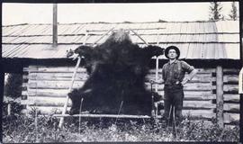 Man with rifle posing next to drying bear skin