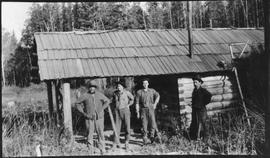 Four men standing in front of a log cabin