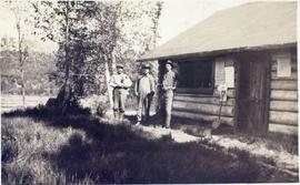 Three men standing in front of a log building