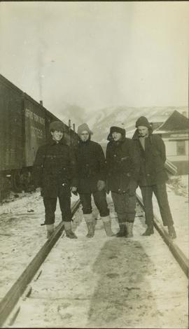 Group photo of four unidentified men posing for a photo on the train tracks