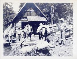 Two men and their horses in front of a cabin
