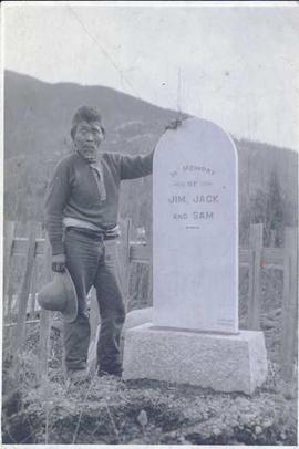 First Nations man standing to the side of a gravestone