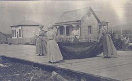 Four women cleaning a rug on a wooden walkway