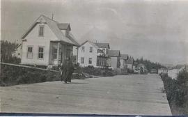 Elderly First Nations woman walking on wooden walkway in front of some houses