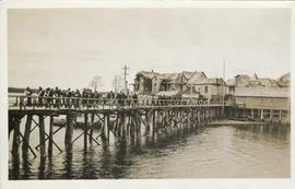 Large group of people walking along a wooden walkway on pilings
