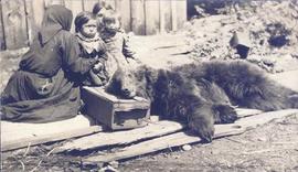 Children and women sitting behind a dead bear
