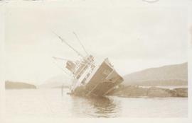 A ship beached on rocks, leaning heavily to the side