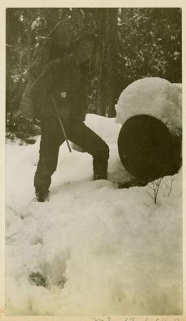 Hiker with pack posing next to a snow-covered log