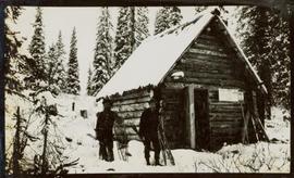 Two men with snowshoes standing in front of a log cabin
