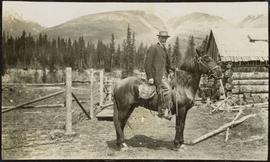 Man on a horse in front of a log cabin