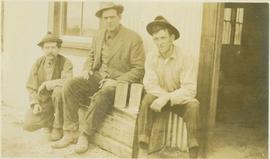 Three men sitting on a bench outside of a building