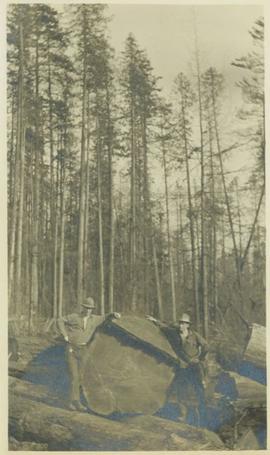 Two men posing beside a very large log