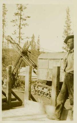 Unidentified man standing on a wooden road beside a steamshovel