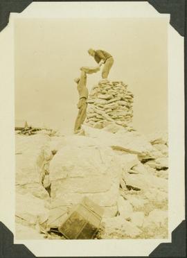 Walter and Skookum building a cairn over a mountain station