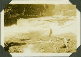 Frank Swannell standing on a rocky shore next to white water rapids